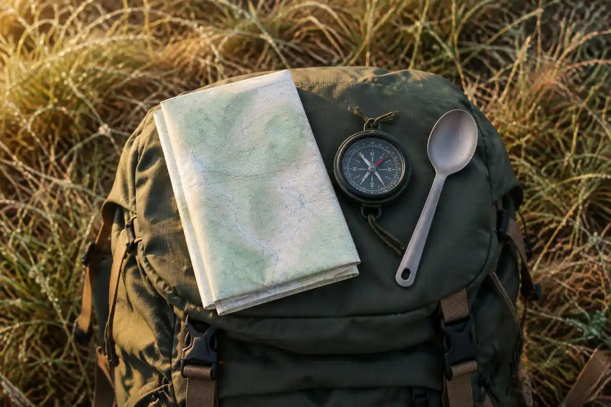 Trail map, small compass and spork laid on a pack lid