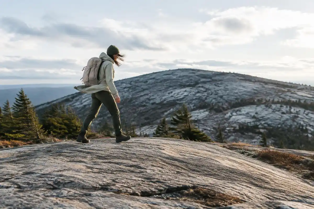 Hiker crossing a bare rock slab in wind with a pale lightweight pack