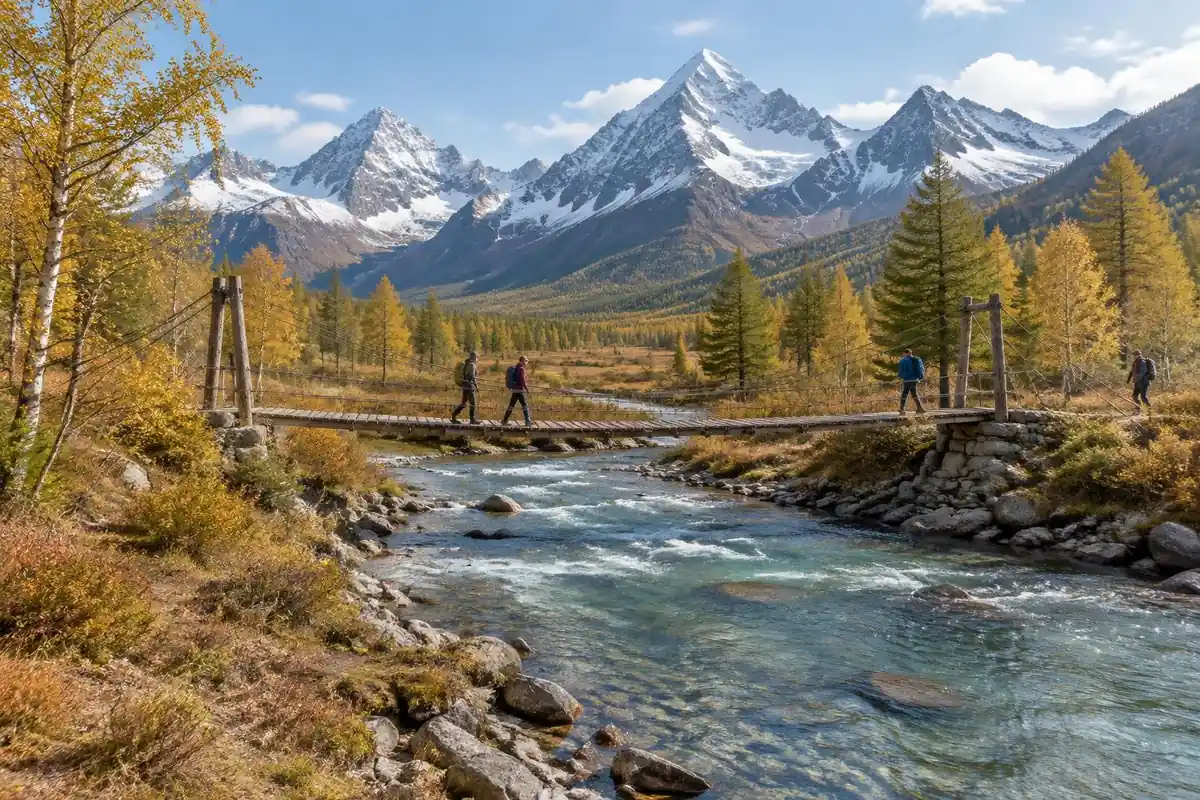 Clear river through a larch valley with a wooden footbridge below sharp peaks