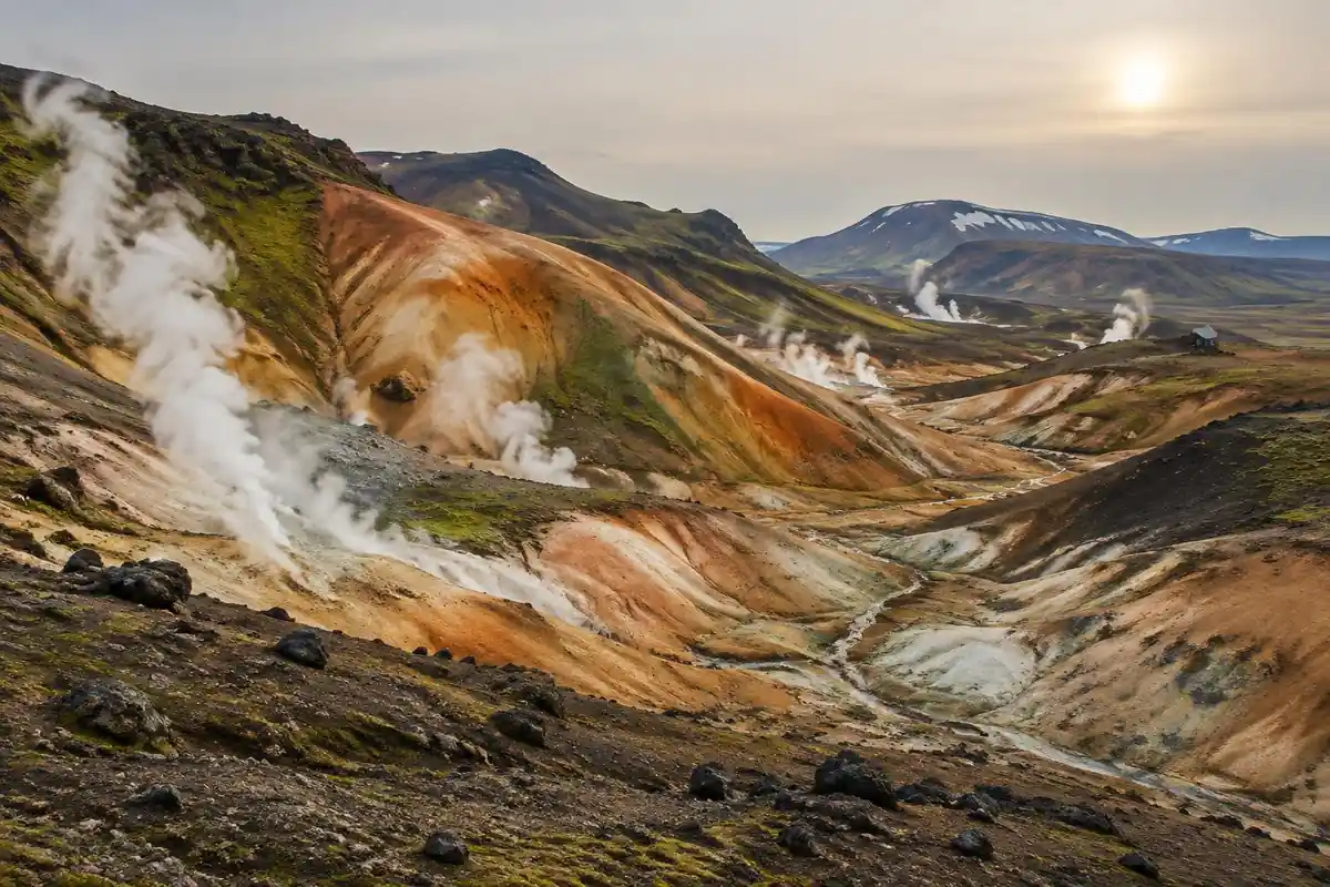 Rainbow rhyolite hills with steam vents and a hut in the distance