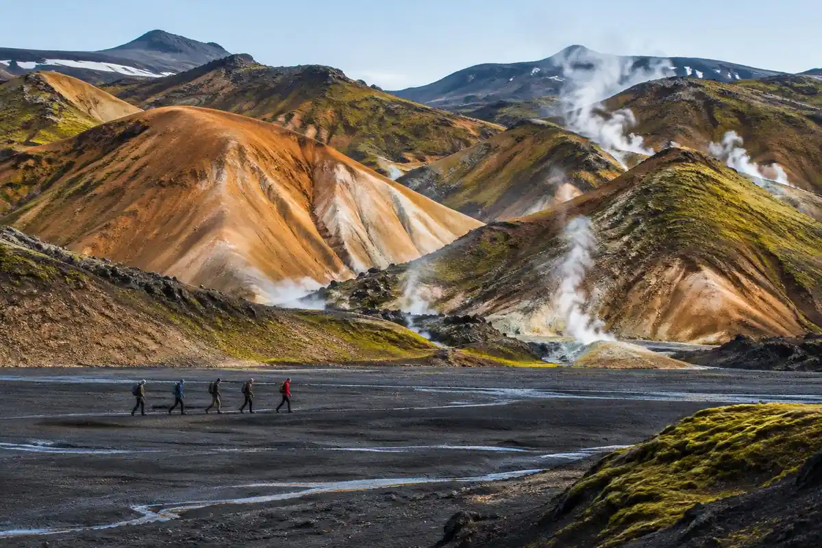 Rhyolite hills in orange, green and blue with steaming vents and black sand plain