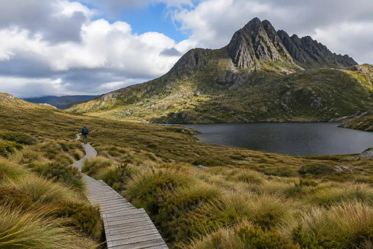 Boardwalk over a button-grass moor toward a jagged mountain and dark tarn
