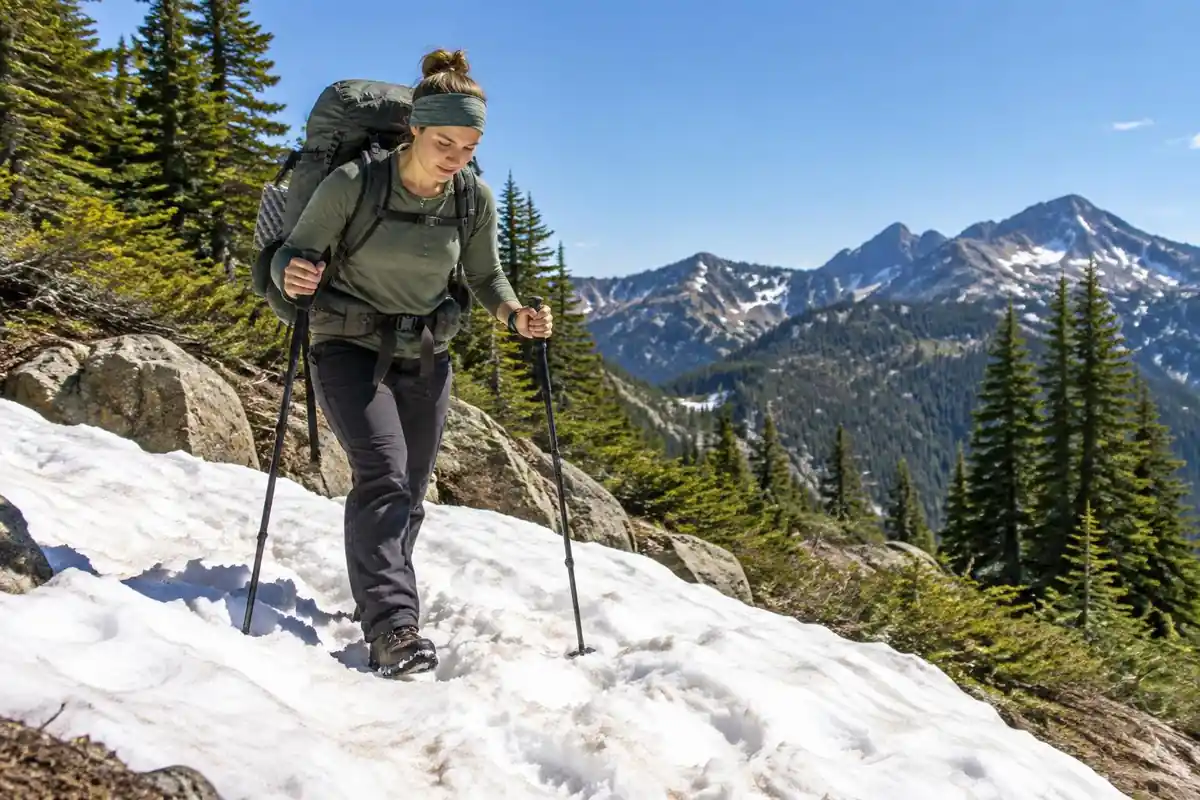Thru-hiker with trekking poles crossing a patch of lingering snow in bright sun