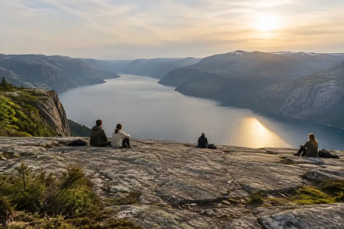 Visitors seated on a broad flat rock plateau high above a steel-blue fjord