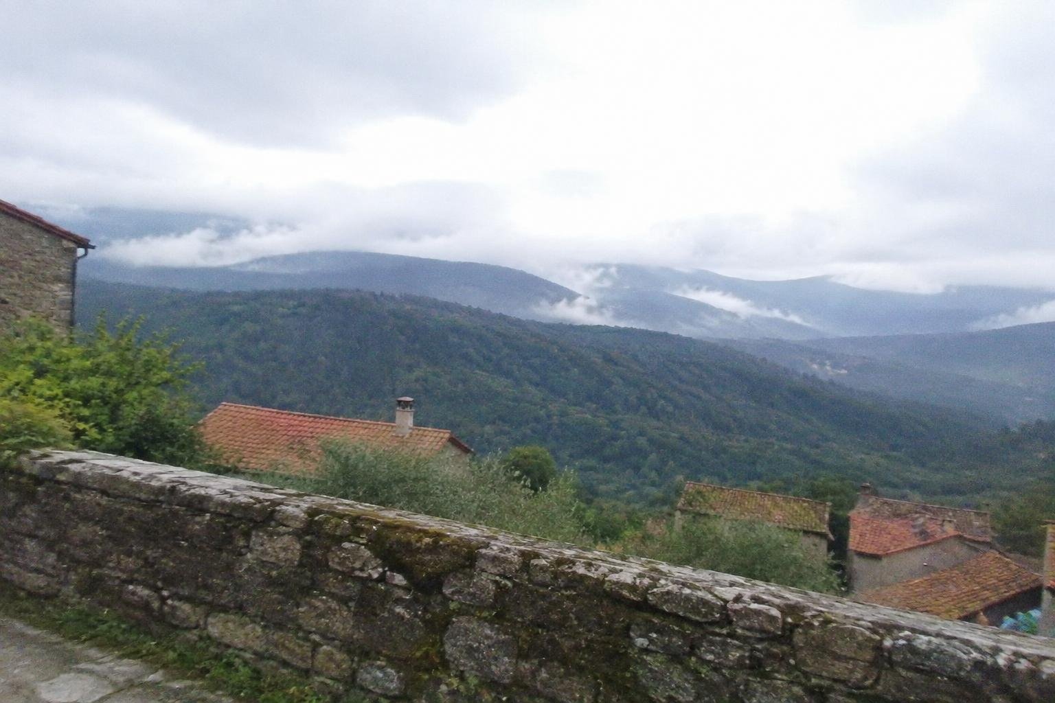 A hillside hamlet with folded ridges and low cloud beyond a stone wall