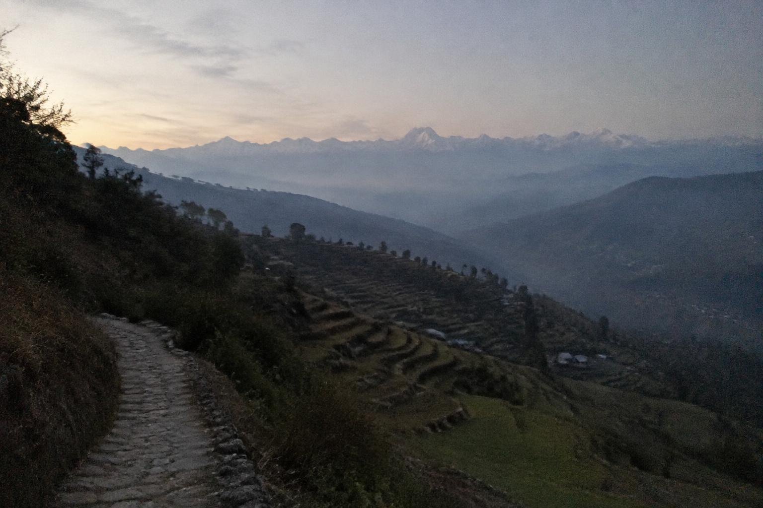 A pale blue valley morning with distant white peaks over terraced hillside
