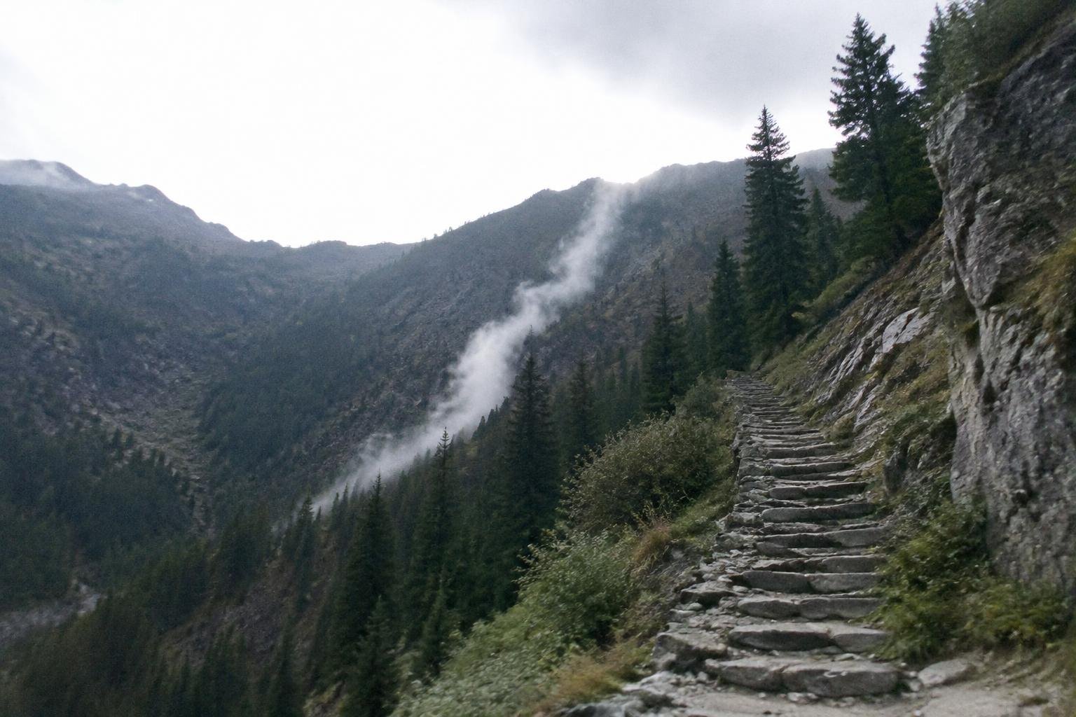A thin white cloud strand drifting up a valley slope