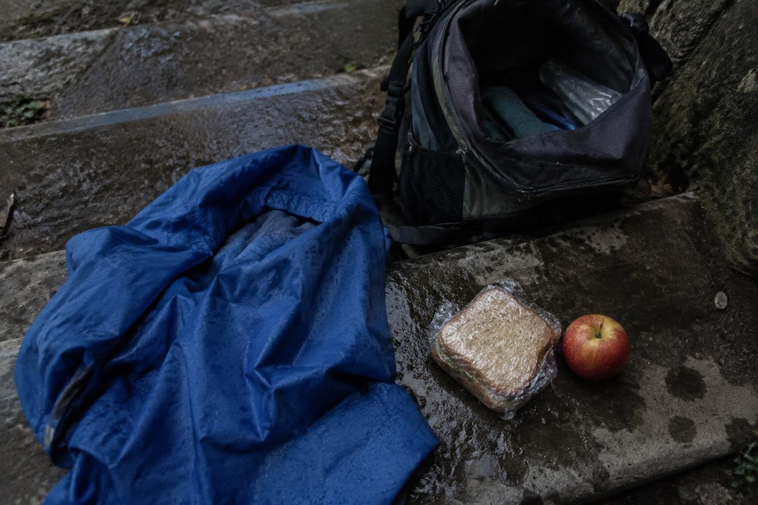 A waterproof shell pulled from the bottom of a pack lying on stones beside a squashed sandwich