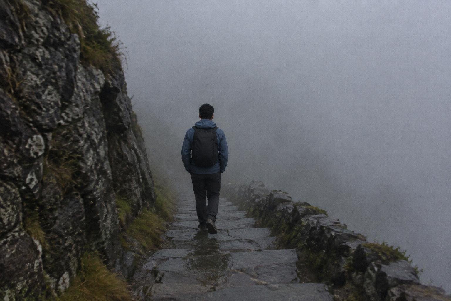 Hiker in a blue shell descending stone steps into thick cloud