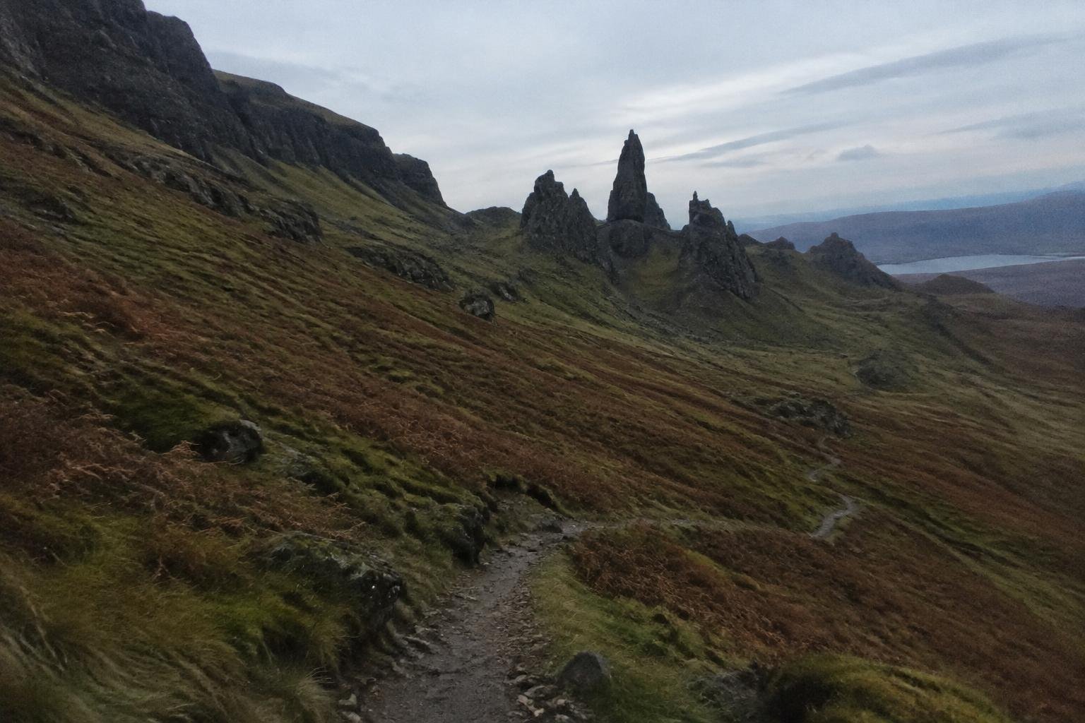 Copper-coloured moorland and jagged summit towers in clear dawn light behind a descending trail