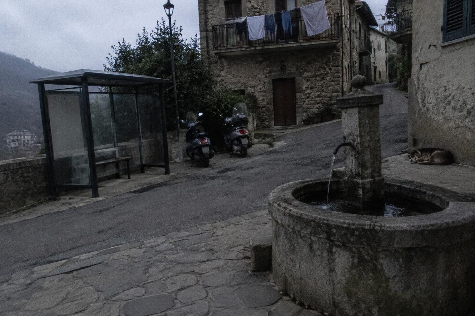 A small village square with a bus shelter and a handful of parked scooters