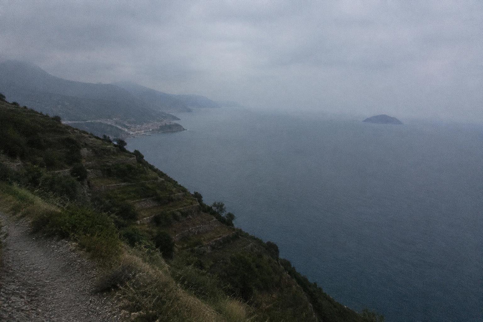 The sea far below the cliff edge with a hazy coastline and an island